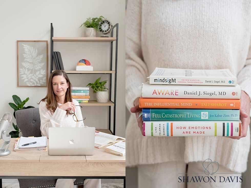 Woman at a desk with laptop in a bright room beside a stack of colorful books on a chair