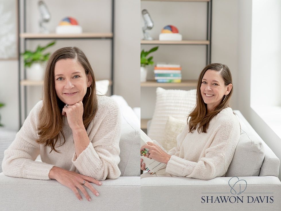 Two women in cream sweaters sitting on a white sofa in a bright living room, smiling at the camera