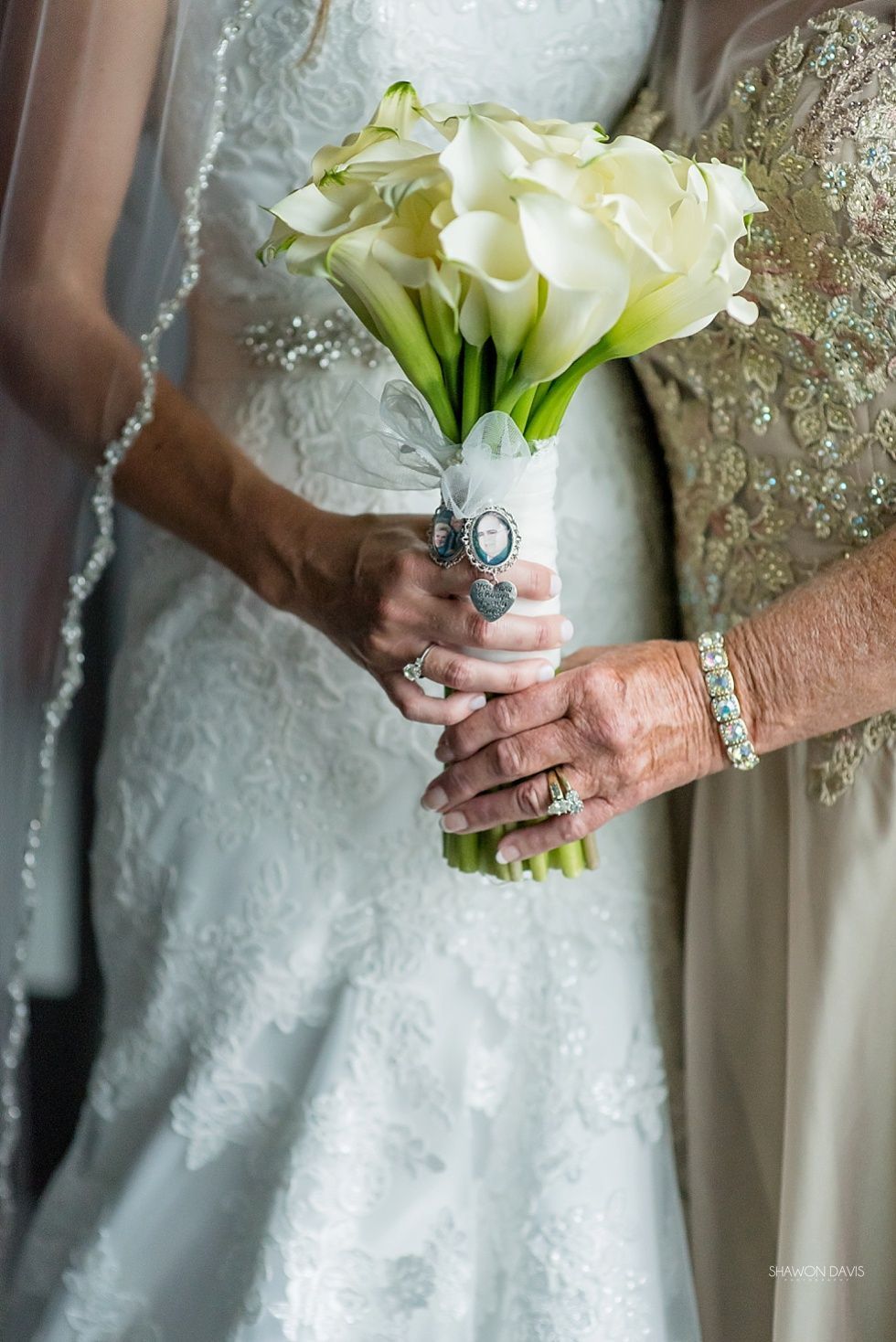Two hands hold a white bridal bouquet, with a silver wedding dress and sequined gown visible.