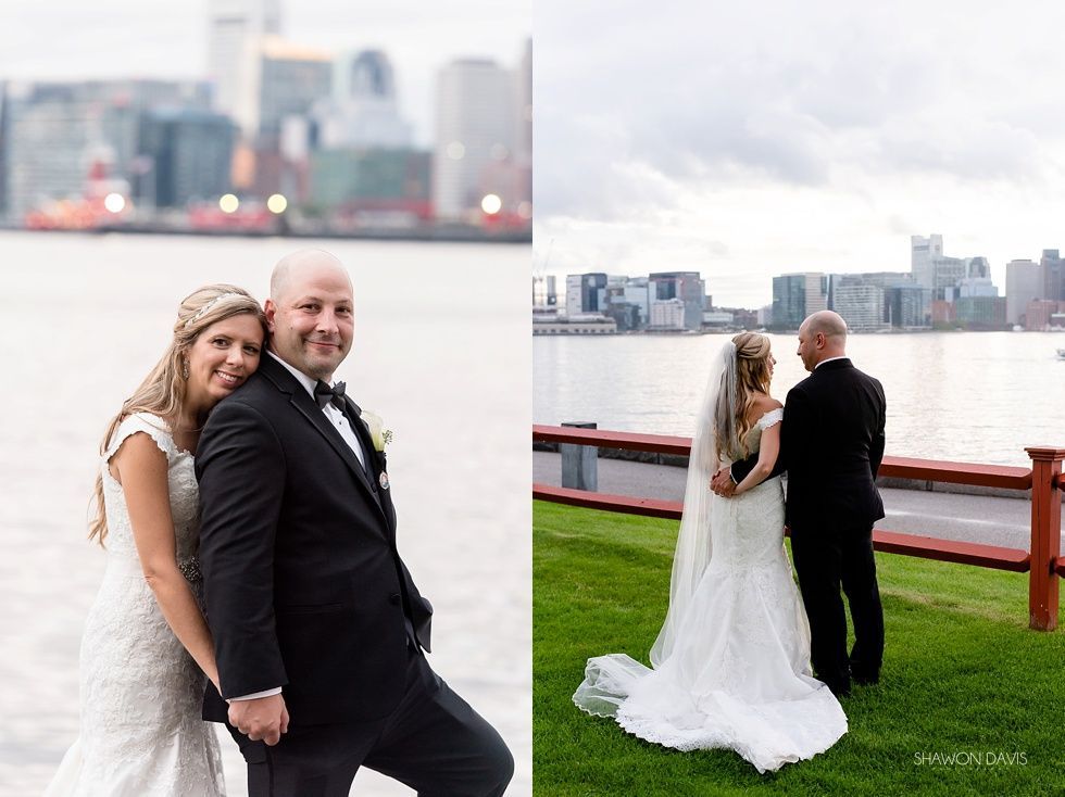 Couple in wedding attire standing by the waterfront with a city skyline in the background