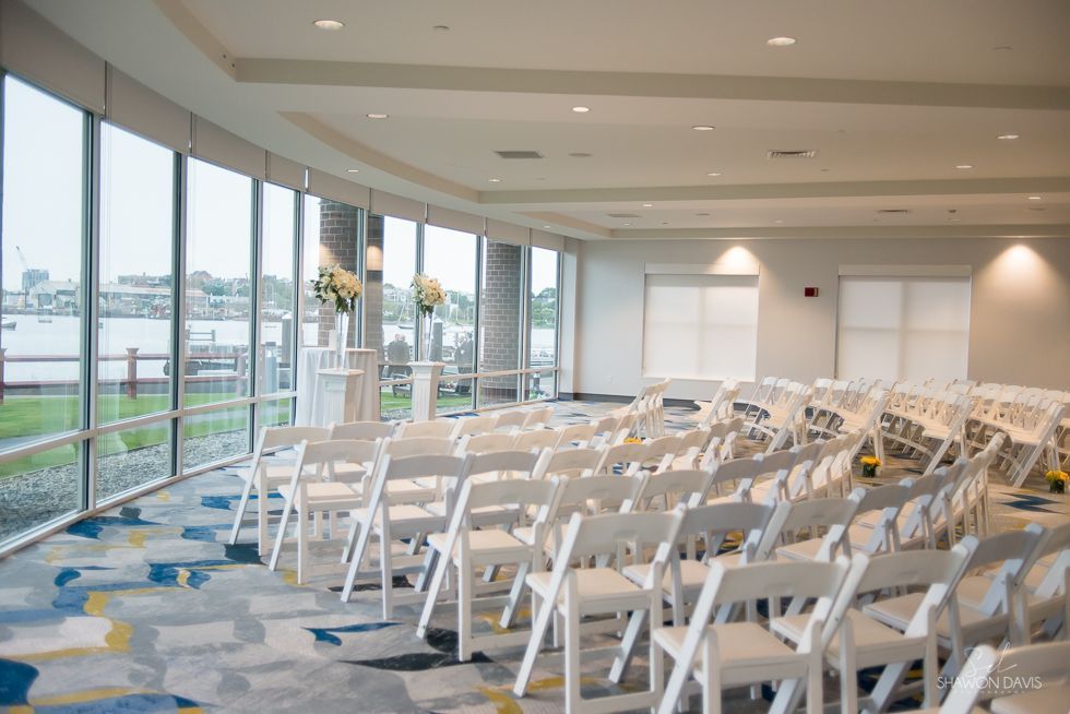 Empty conference room with rows of white chairs facing windows and a carpeted floor