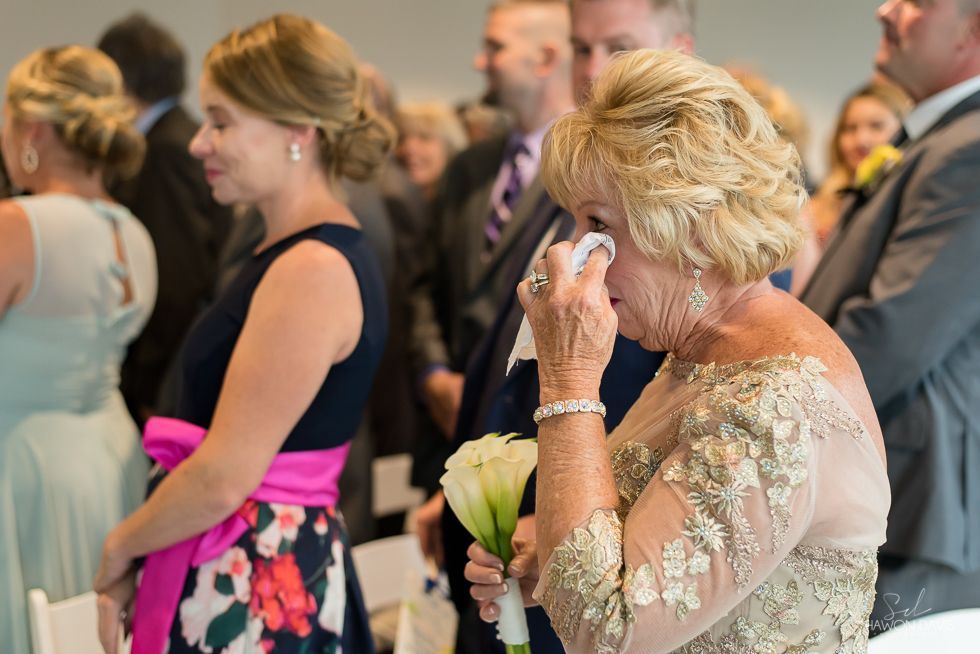 Woman in a floral dress wiping away tears at a formal event while others stand nearby