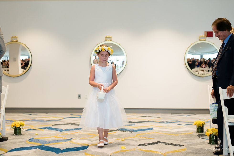 Flower girl stands in a white dress at a wedding ceremony with circular mirrors on the wall.