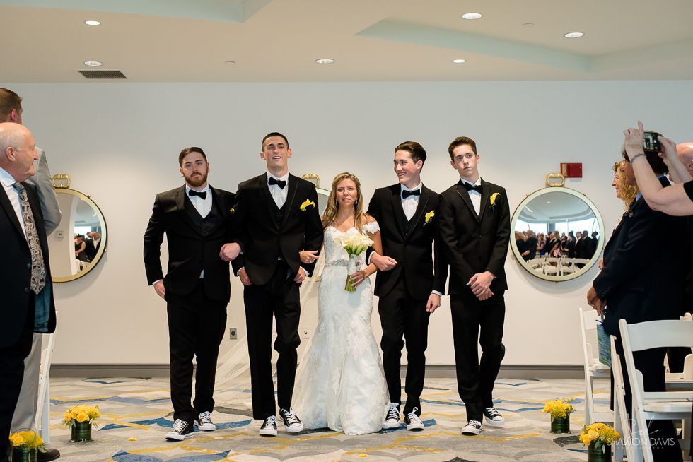 Wedding party posed on a dance floor, bride in white dress with four groomsmen in black tuxedos