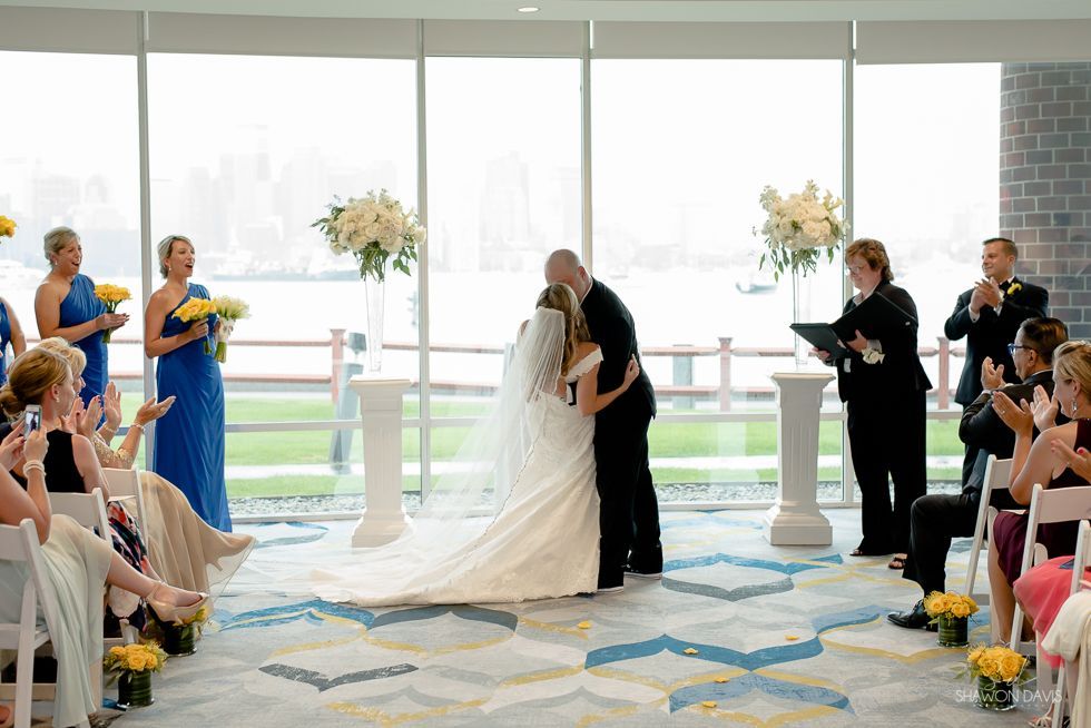 Wedding ceremony in a bright venue, bride and groom at the altar with guests seated on both sides.