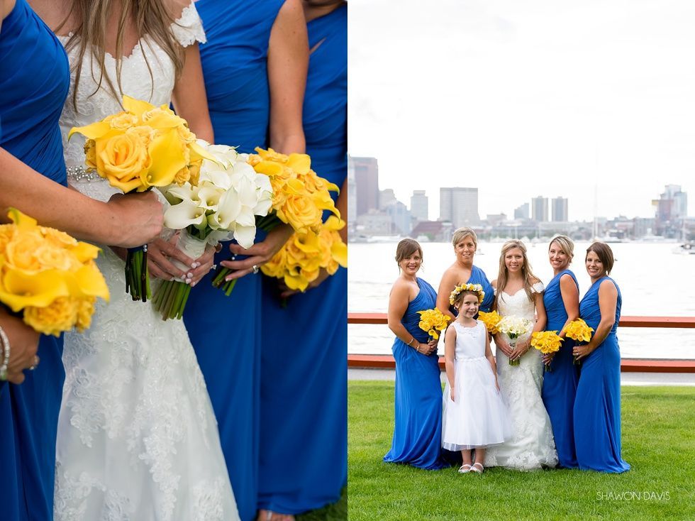 Bridesmaids in blue dresses holding yellow bouquets beside a bride on a waterfront with city skyline