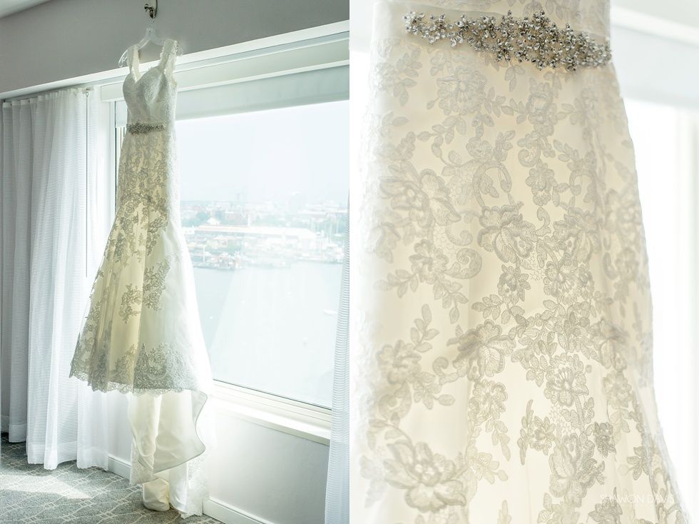 Two lace wedding dresses hanging by a bright window with a city view