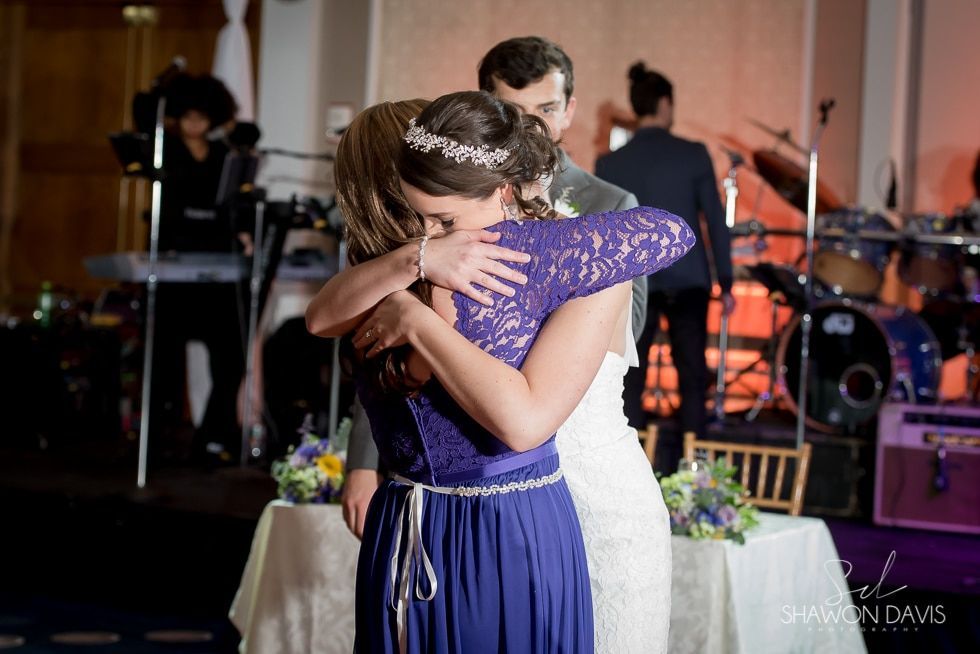 Two people in formal dresses hugging during a slow dance at a reception, with a live band in the background.