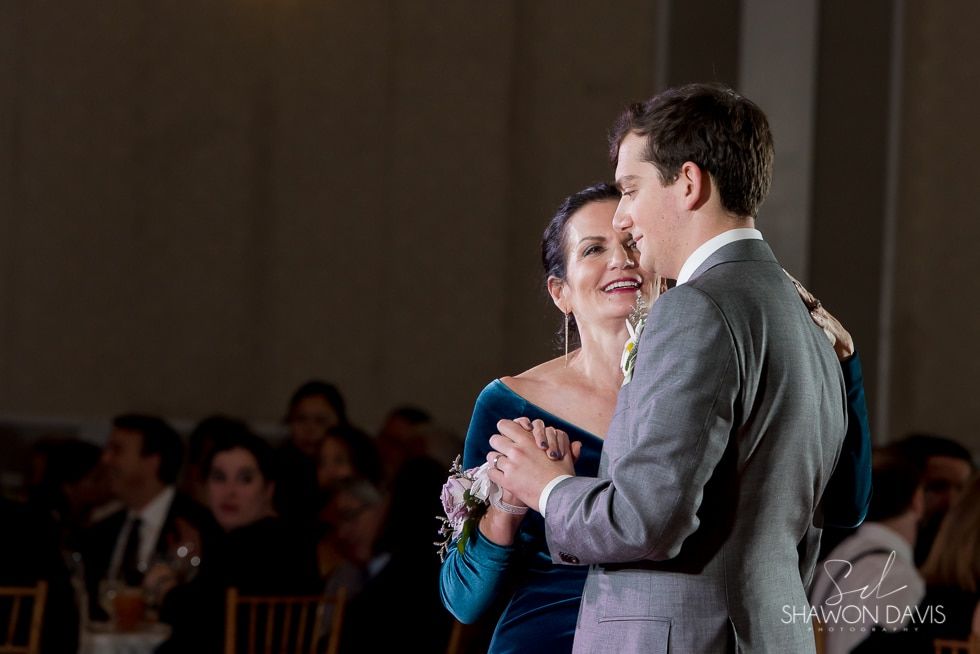 A couple dancing closely at a formal event, the woman in a blue dress and the man in a gray suit.