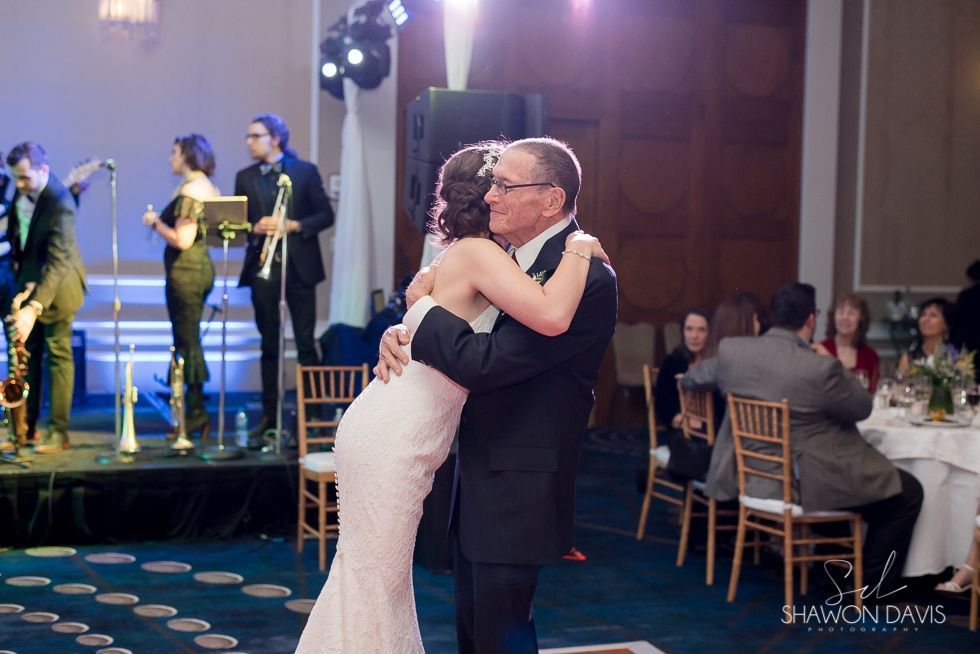 Couple slow dancing at a wedding reception while a live band performs onstage nearby