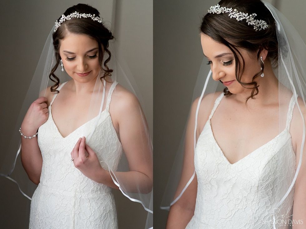 Woman in a white dress with a veil and tiara, looking down and adjusting her dress.