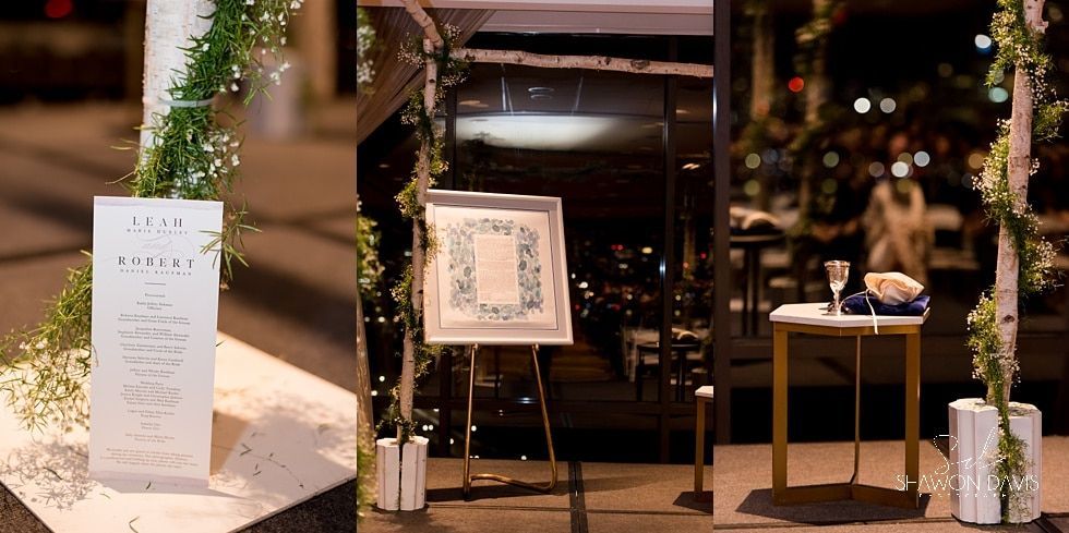 Indoor event display with easel signs, floral arrangements, and a small table under warm lights