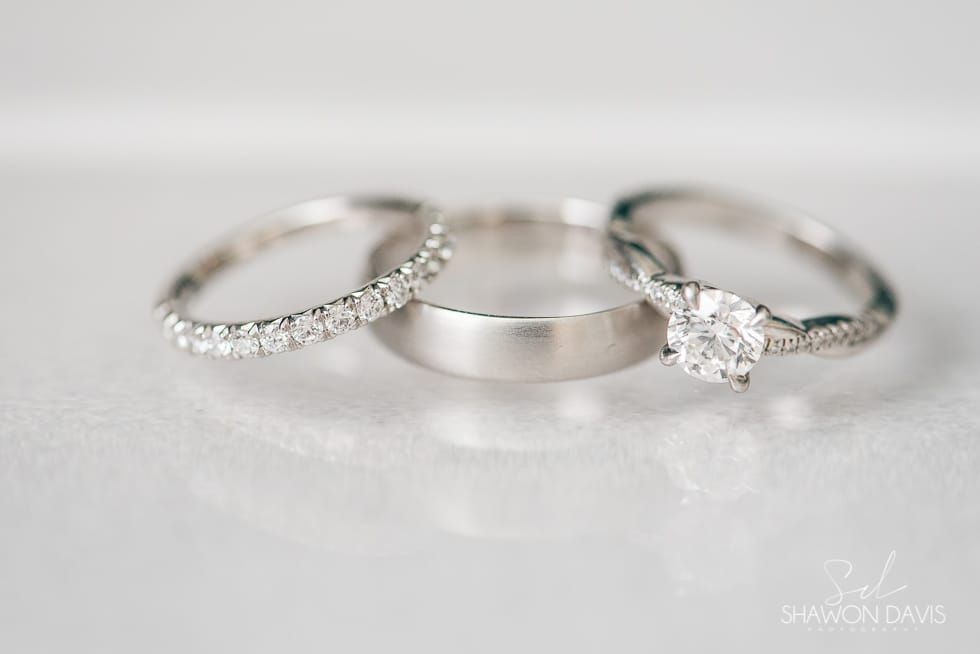 Three silver rings on a white surface, including one diamond-studded band and one solitaire ring