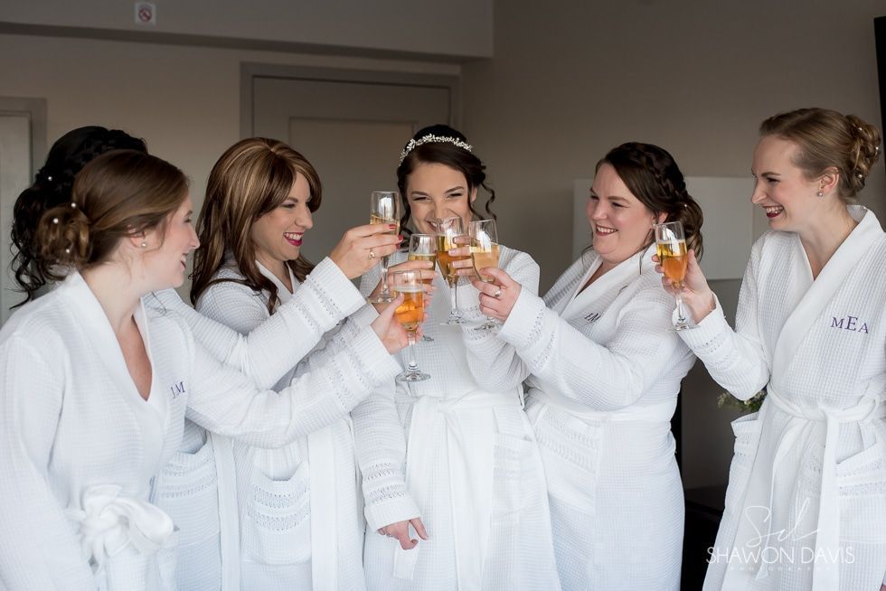 Five people in white robes toast champagne glasses indoors, smiling.
