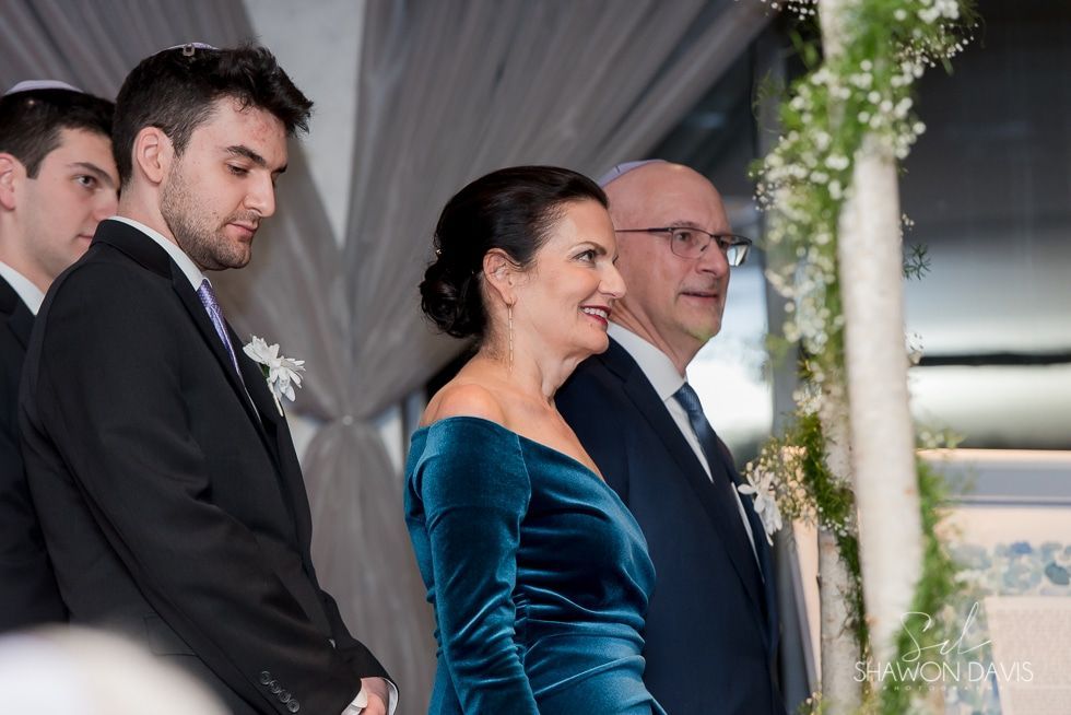 Guests in formal attire smiling at an indoor wedding ceremony