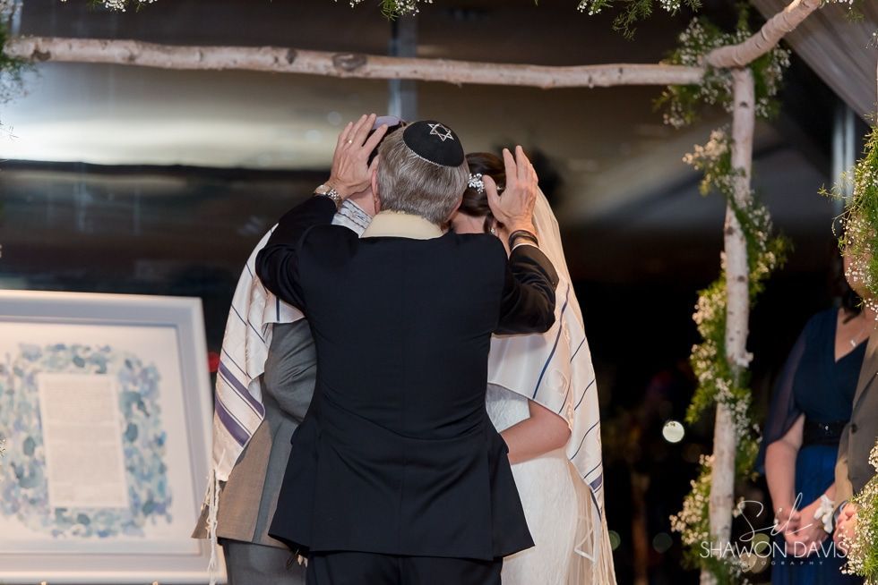 Couple embracing at an indoor wedding ceremony under a flower-covered arch