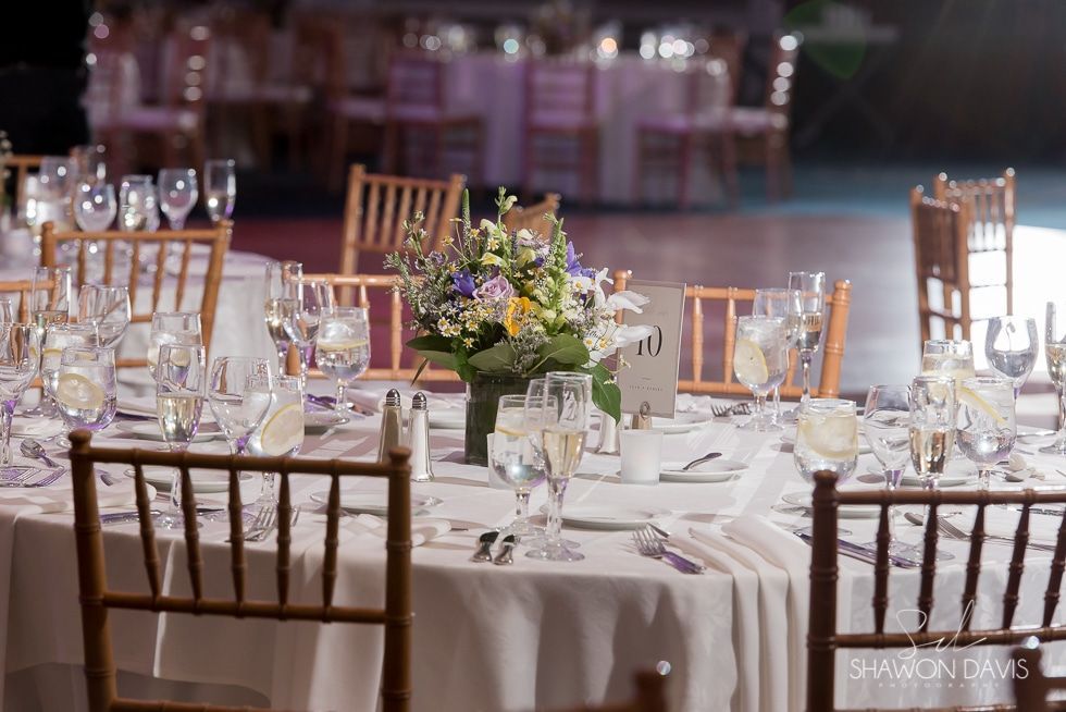 Round banquet tables set with glassware and flowers in a softly lit reception hall.