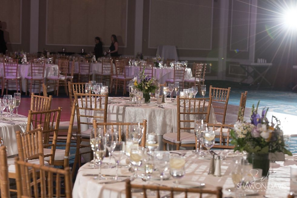 Elegant banquet hall with round tables, gold chairs, white tablecloths, and floral centerpieces in dim lighting