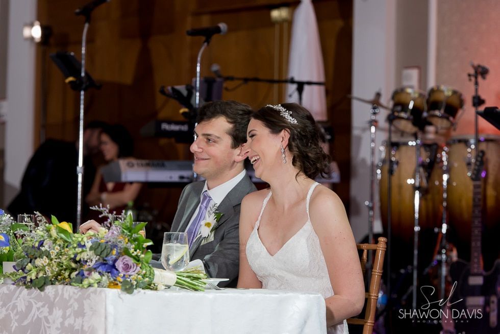 Bride and groom smiling at a decorated reception table with flowers and glasses