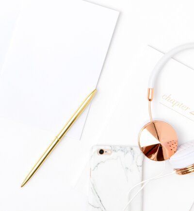 White desk with gold pen, marble phone case, and rose gold glasses on a clean background