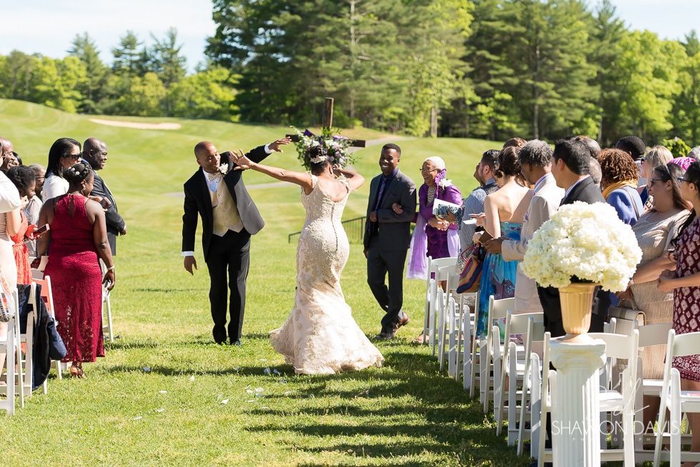 Outdoor wedding ceremony with bride in white dress walking down an aisle lined with guests and white chairs