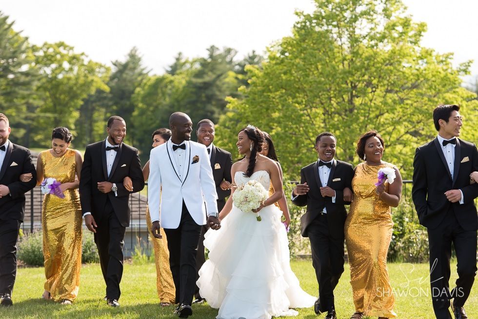 Wedding party walking outdoors on a grassy lawn, with the bride in white and groom in a white tuxedo.