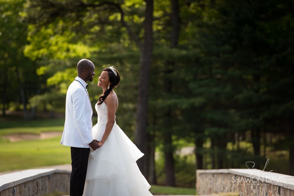 Bride and groom face each other on a stone bridge in a green park.