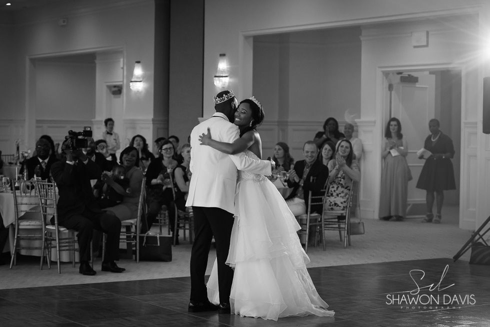 Bride and groom share a dance at a wedding reception, surrounded by seated guests.
