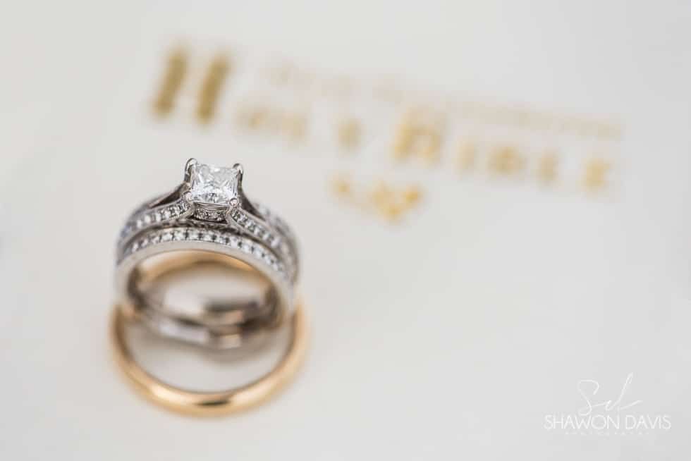 Two wedding rings, one silver diamond ring atop a gold band on a blurred branded card