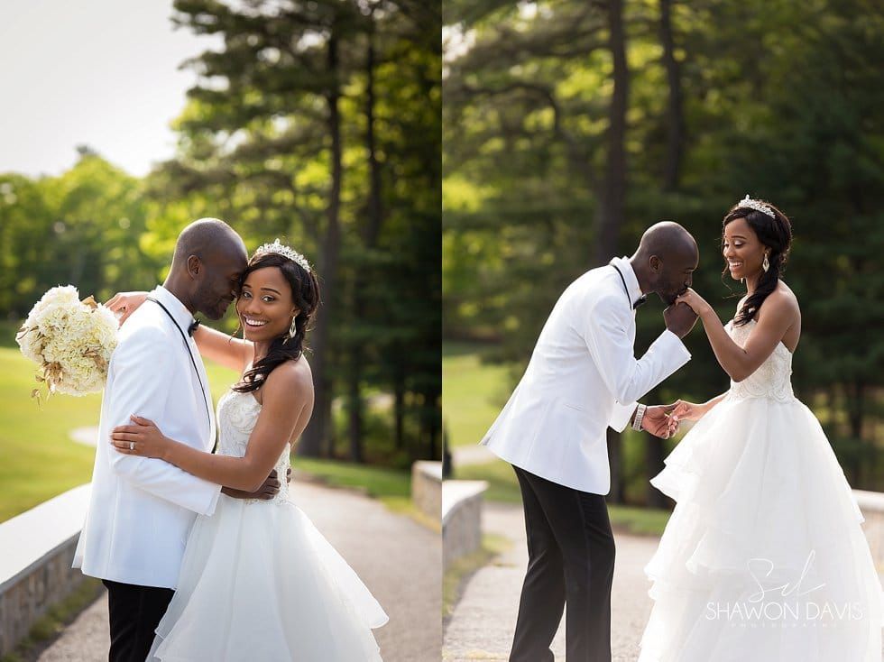 Two wedding couples in white embrace outdoors on a sunlit path with trees in the background