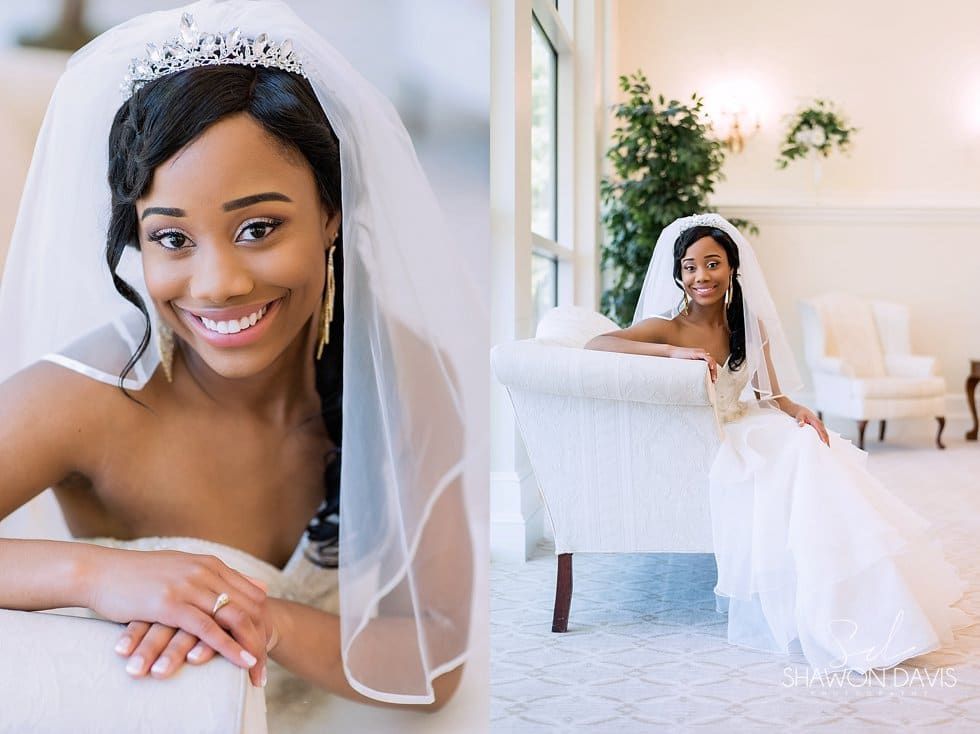Bride in a white gown and veil smiling in a bright, elegant room with a seated portrait and full-length view.