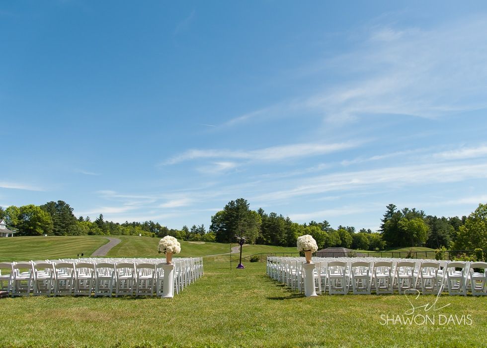 Rows of white chairs set on a grassy field under a bright blue sky, ready for an outdoor ceremony