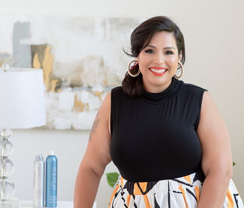Smiling woman in a black top standing in a bright, modern room with abstract wall art and a lamp
