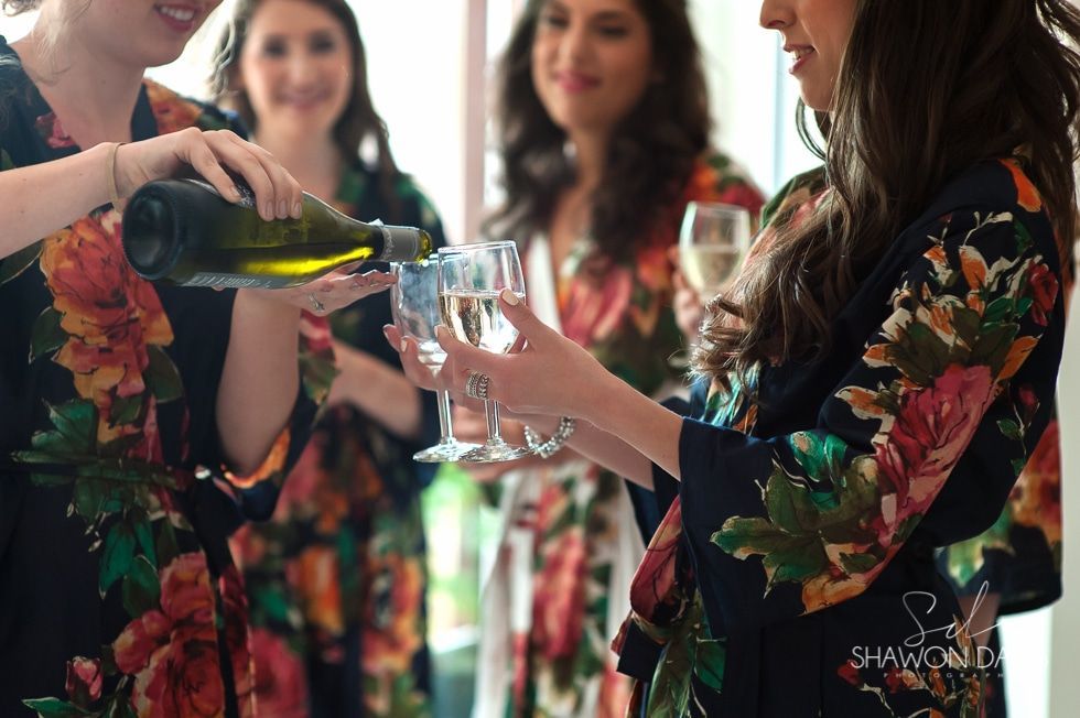 Guests in floral robes pour champagne into glasses at a lively indoor celebration.