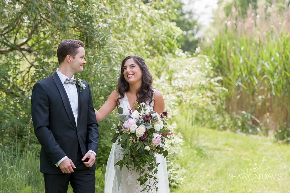 Bride and groom walking outdoors in a garden, smiling and holding flowers