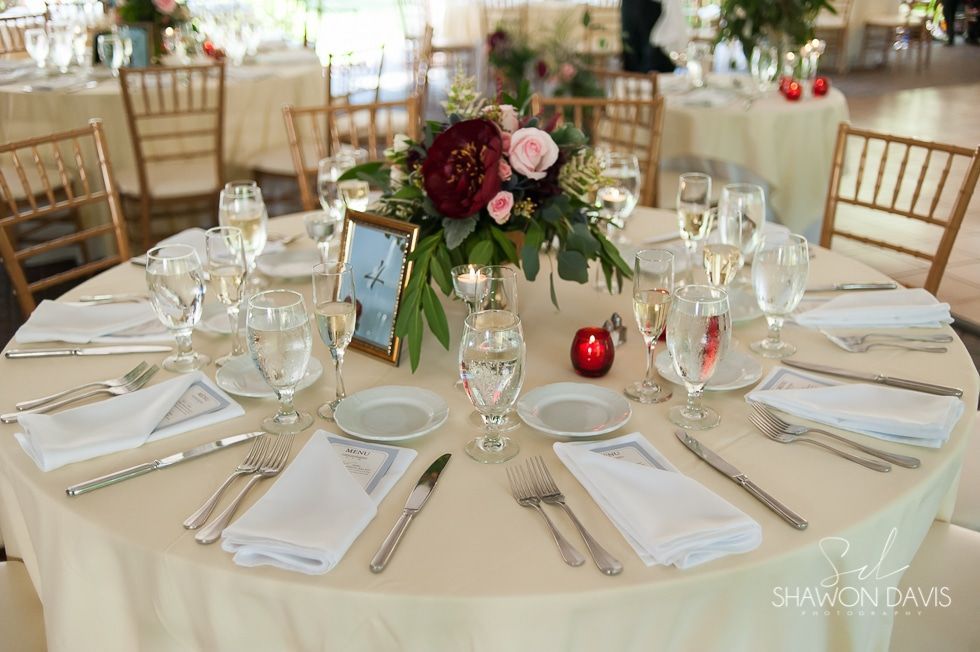 Elegant wedding reception table with white linens, glassware, floral centerpiece, and red candle accents