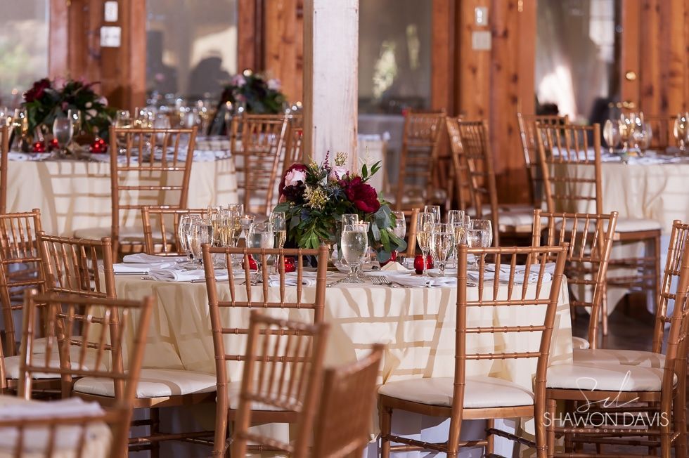 Elegant banquet hall with round tables, gold chairs, white linens, and red floral centerpieces
