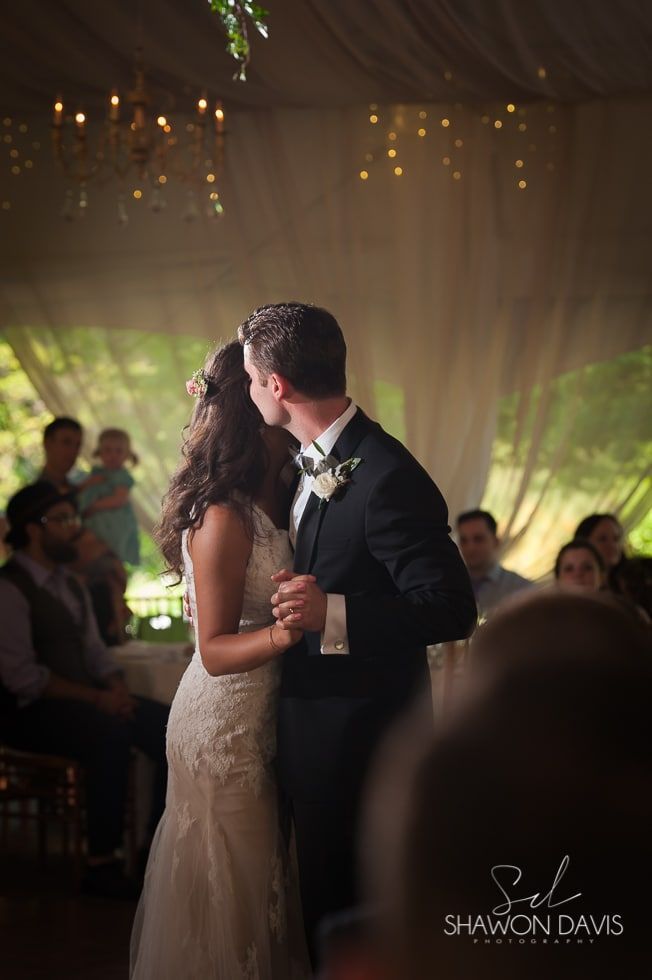 Bride and groom kissing at their wedding reception under warm string lights