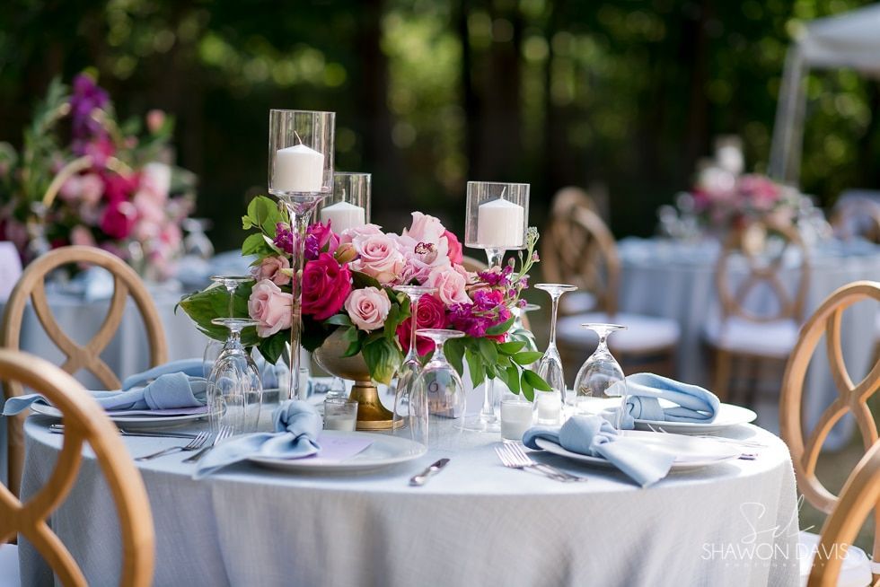 Elegant outdoor table set with pink floral centerpiece, candles, and blue napkins at a wedding reception