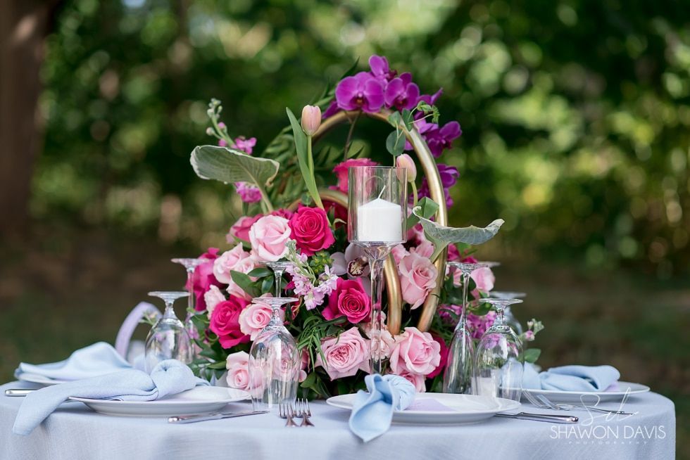Floral centerpiece with pink roses and candles on a white table with pale blue napkins outdoors