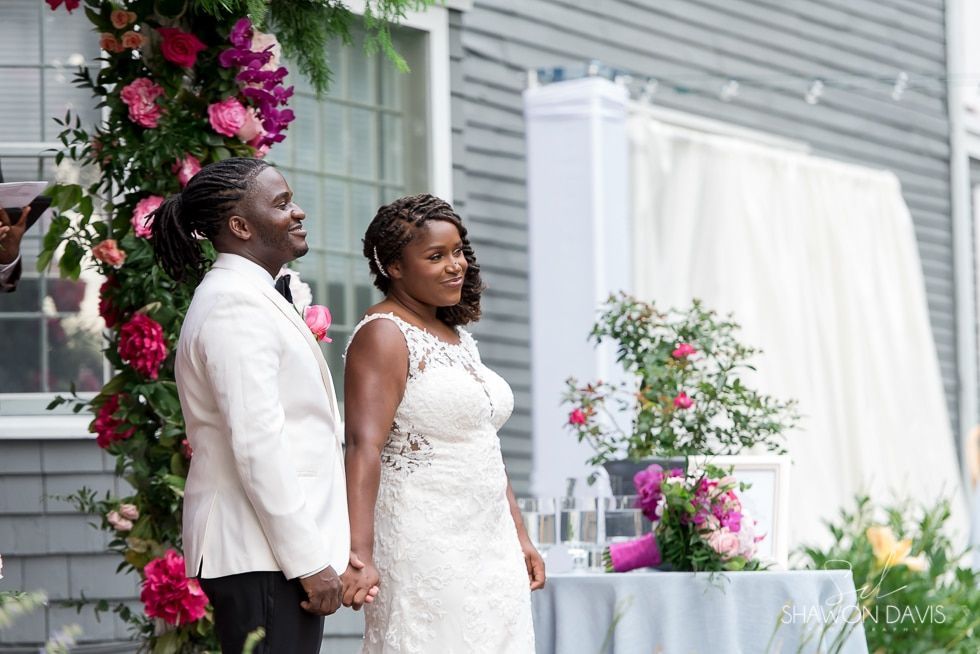 Newlyweds standing beside a floral wedding arch and table outdoors