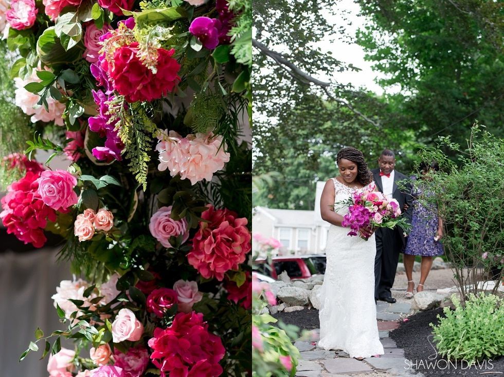 Bride and groom walking down a flower-lined garden aisle at an outdoor wedding