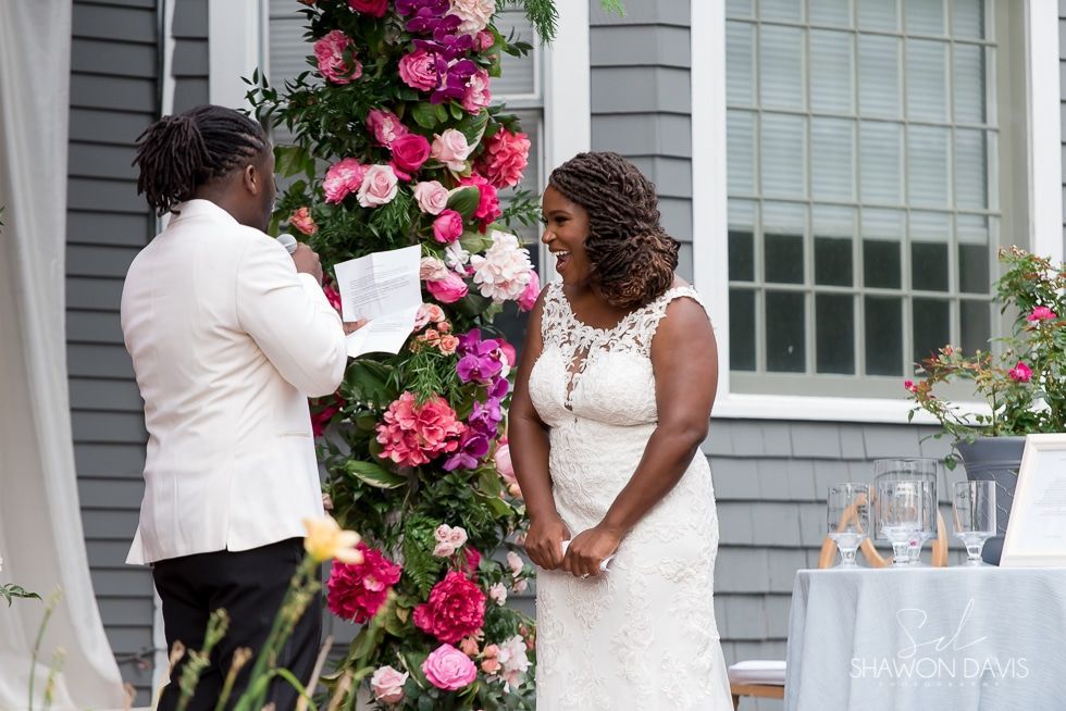 Wedding ceremony by a flower wall, with the couple exchanging vows beside a decorated table.