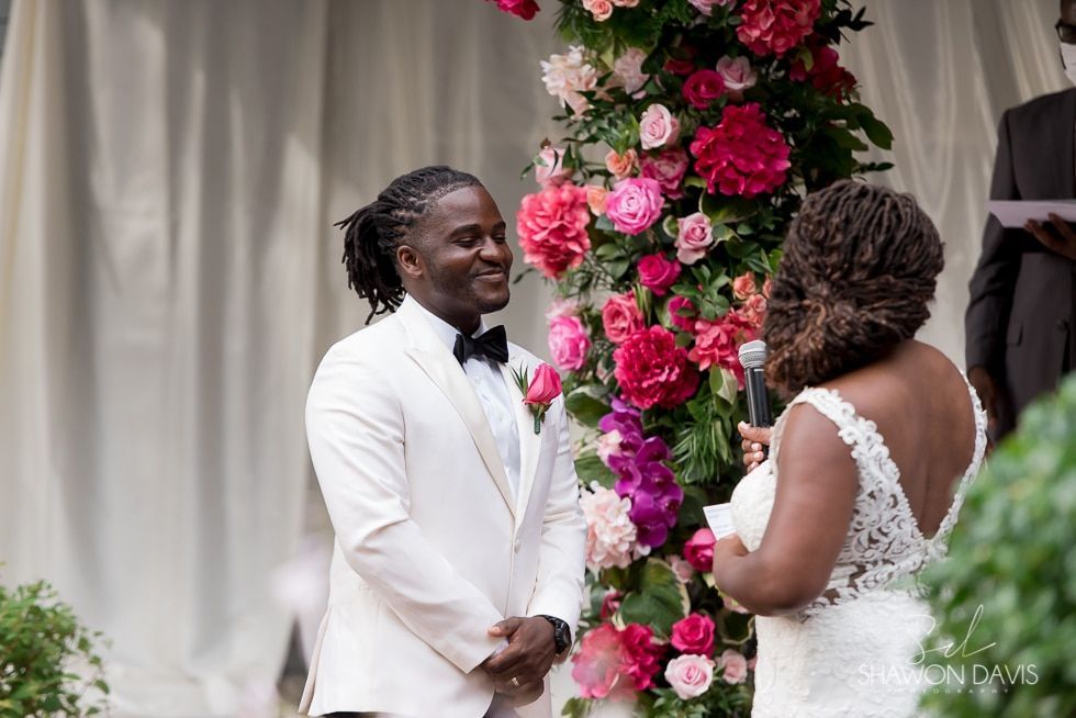 Bride and groom exchanging vows beneath pink floral arch at an outdoor wedding ceremony