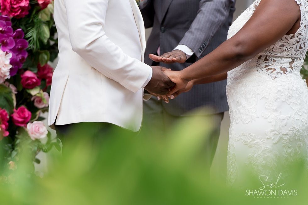 Wedding couple holding hands beside pink flowers in an outdoor ceremony