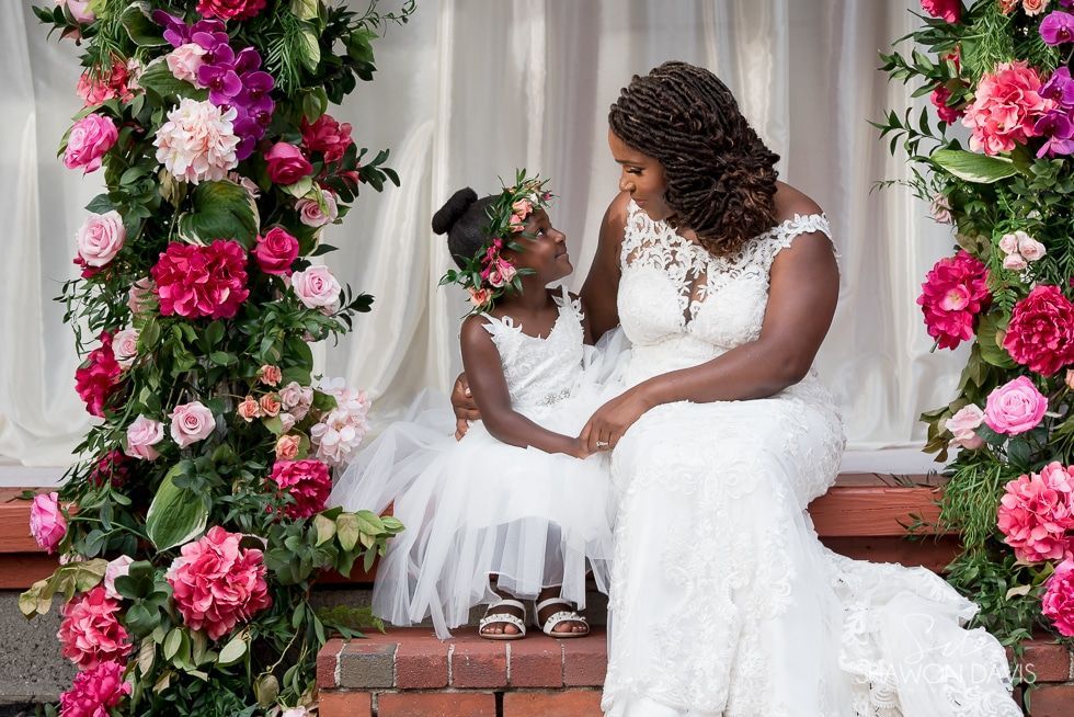 Bride and young girl in white dresses seated on a floral-decorated wedding step
