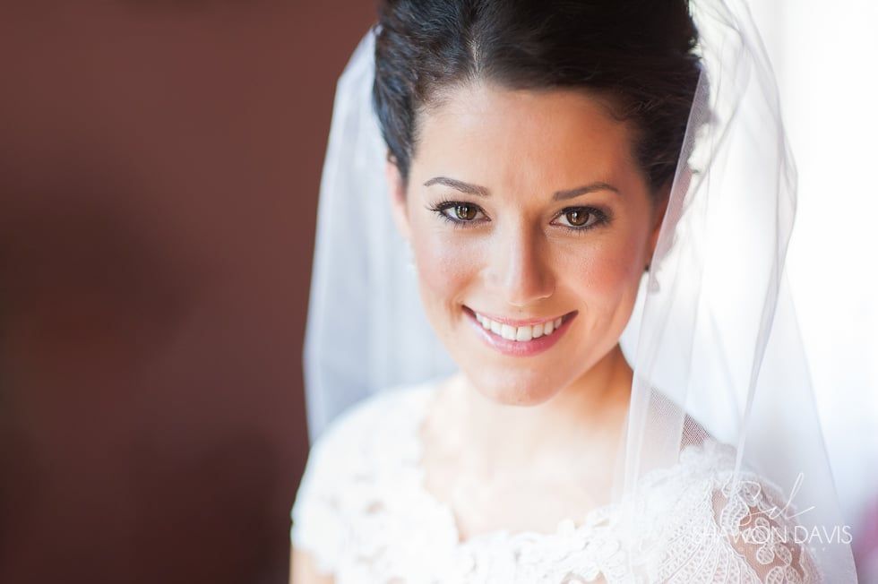 Smiling bride in a white veil, softly lit against a blurred background