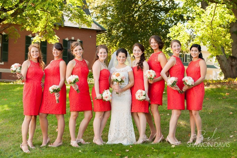 Bride with bridesmaids in red dresses standing outdoors under trees
