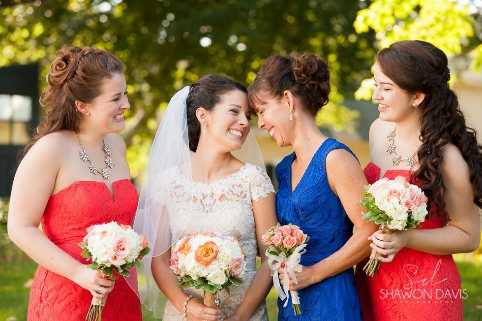 Four bridesmaids in colorful dresses holding bouquets and smiling outdoors at a wedding.