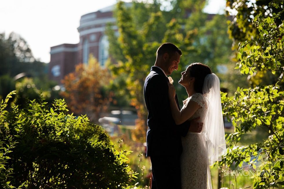Silhouetted couple embracing outdoors in a sunlit garden with city buildings in the background